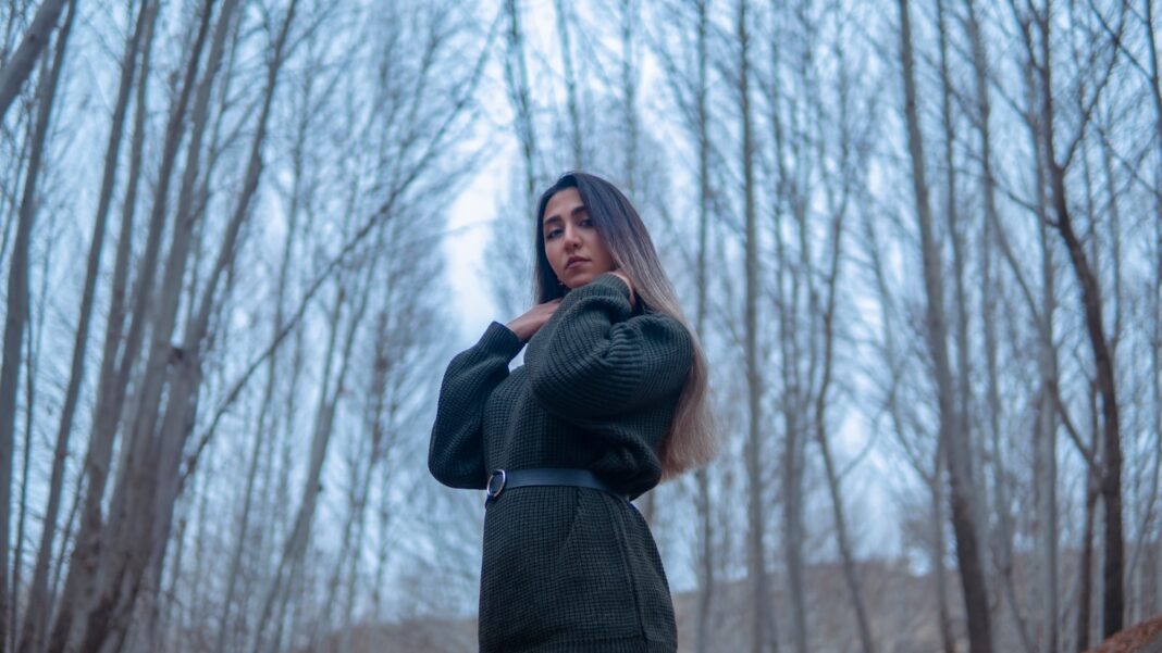 a woman standing in a forest with trees in the background